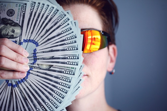 A hand holding a fan of U.S. hundred-dollar bills, symbolizing wealth, market activity, and the importance of staying updated with live financial news.