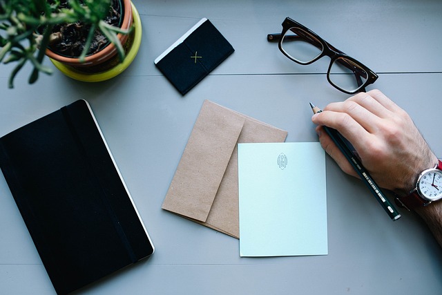 *Four Basic Tax Planning Variables*—A person writing on paper with a pen at a neatly organized desk, surrounded by a notebook, envelopes, glasses, and a small plant, symbolizing financial documentation, tax strategy, and structured planning.